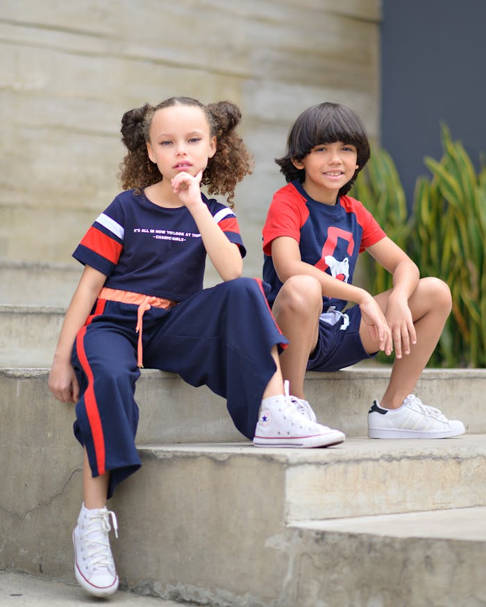 Two children in sporty outfits sitting on outdoor stairs, exuding youthful energy and style.